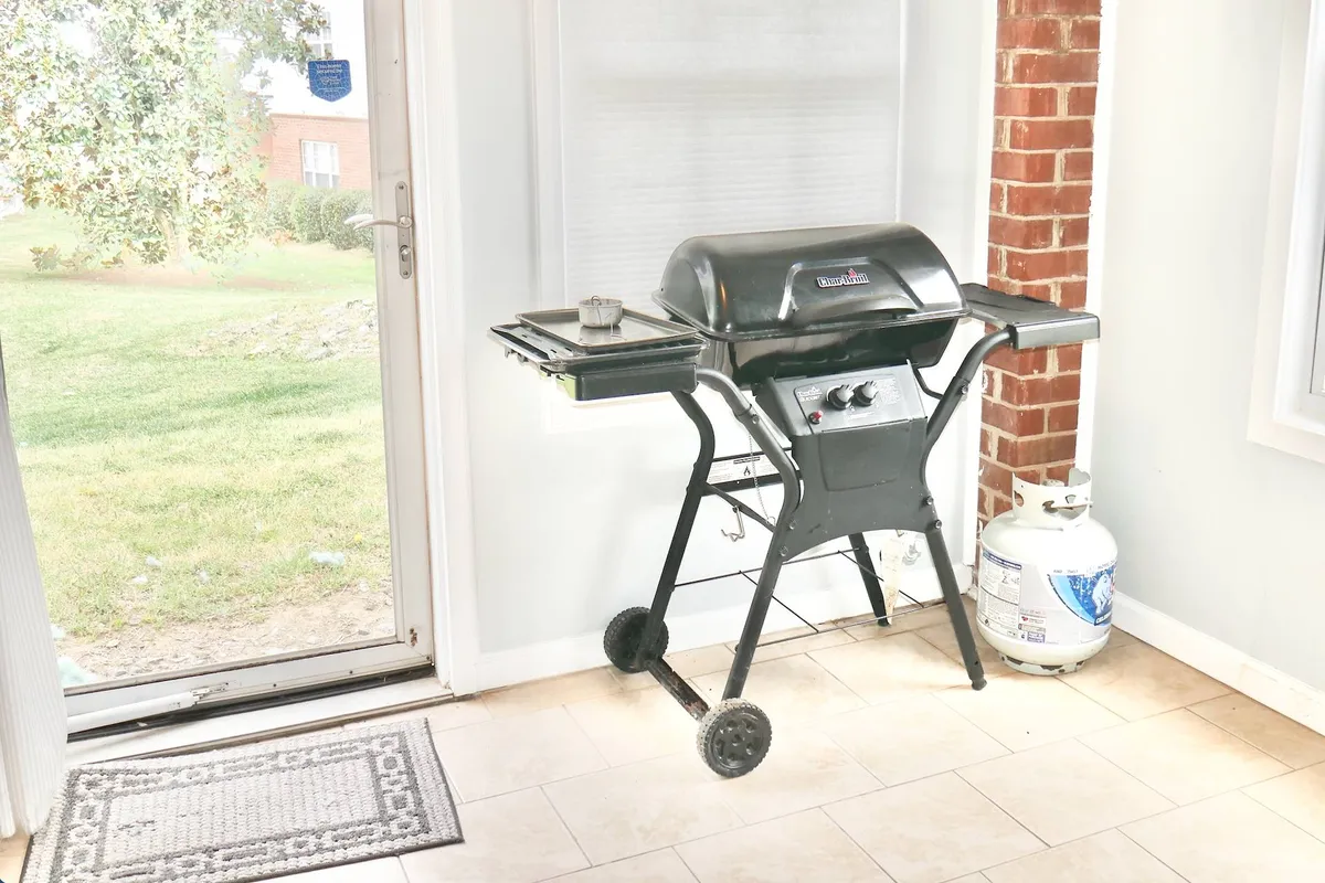 An interior scene featuring a private propane grill with a propane tank, placed near a doorway—suggesting easy access to outdoor grilling. The setup conveys a casual, inviting atmosphere ideal for barbecuing, entertaining, and enjoying meals al fresco.