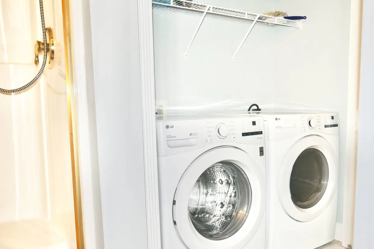 A utility room with a washer and dryer stacked beside a shower, providing efficient space for laundry chores and quick clean-ups. The space is neat and functional, emphasizing convenience for extended stays.