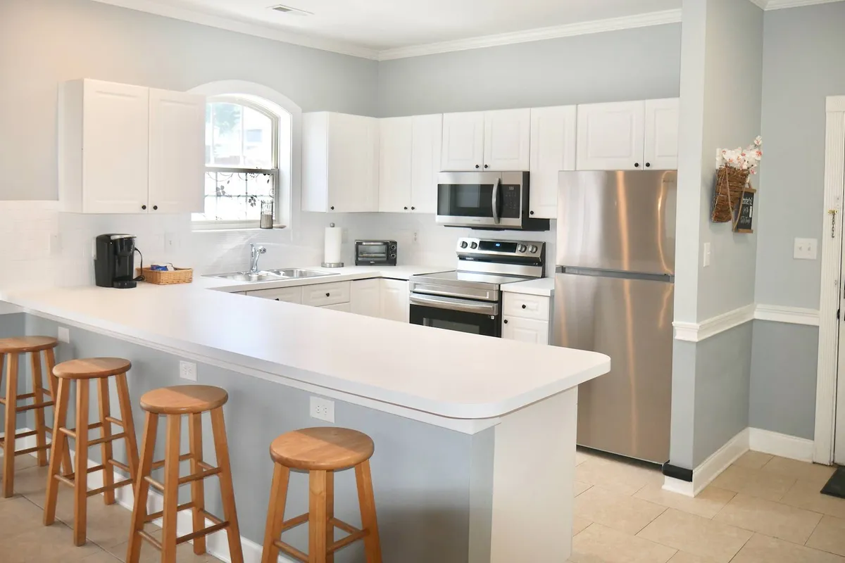 A stylish, modern kitchen with a prominent island, sleek stainless steel appliances, white cabinetry, and inviting stools. The scene exudes a welcoming, functional vibe ideal for cooking, entertaining, and casual meals.