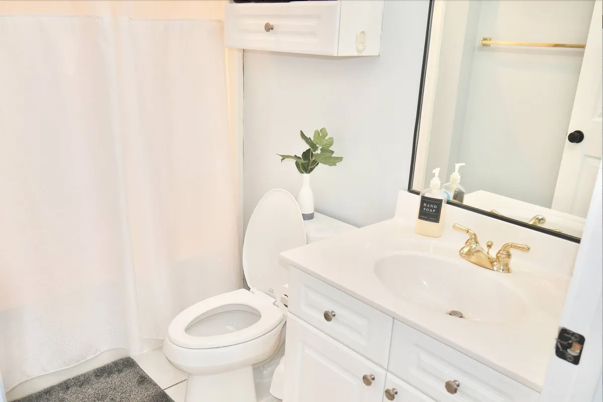 A clean, calming bathroom with a contemporary sink featuring a gold faucet, a small plant, a toilet, and a stylish mirror. The overall design is modern and spa-like, perfect for relaxation and self-care.