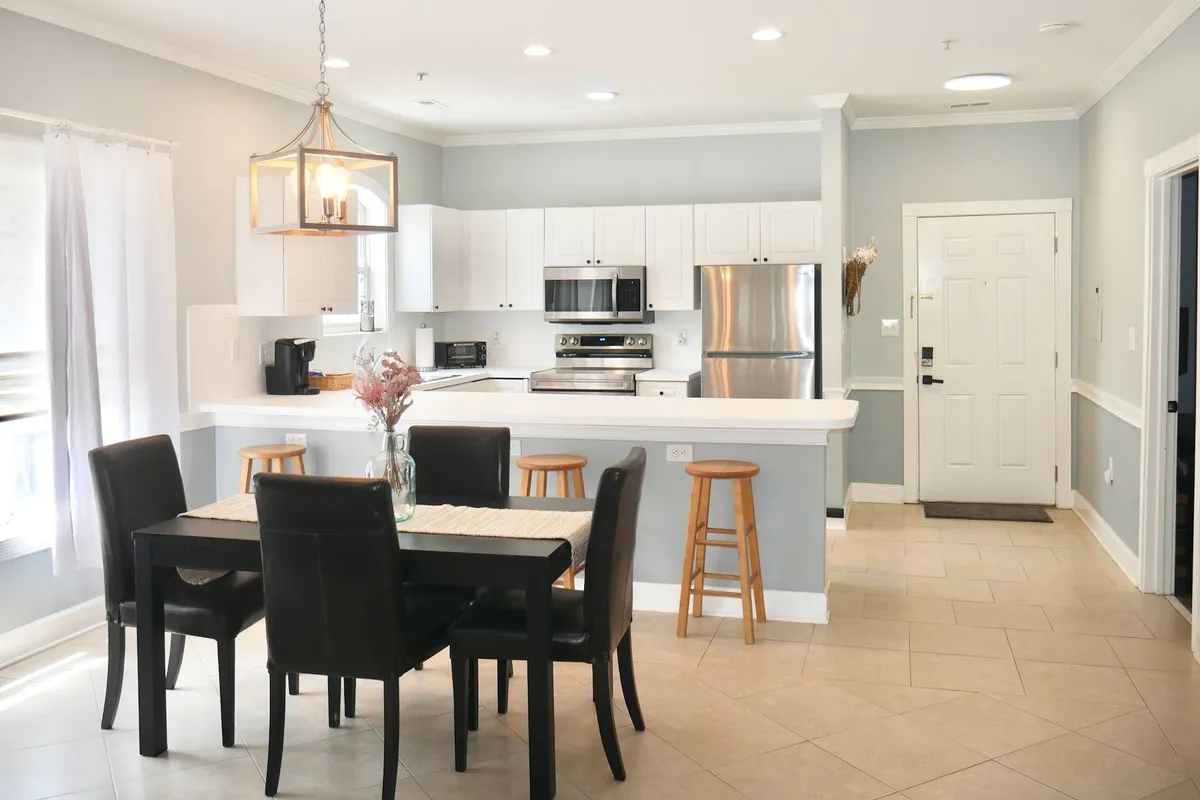 A bright, inviting open concept dining and kitchen area featuring a dining table set for meals, a kitchen island with stools, and stainless steel appliances. The space is styled for both family gatherings and casual entertaining.