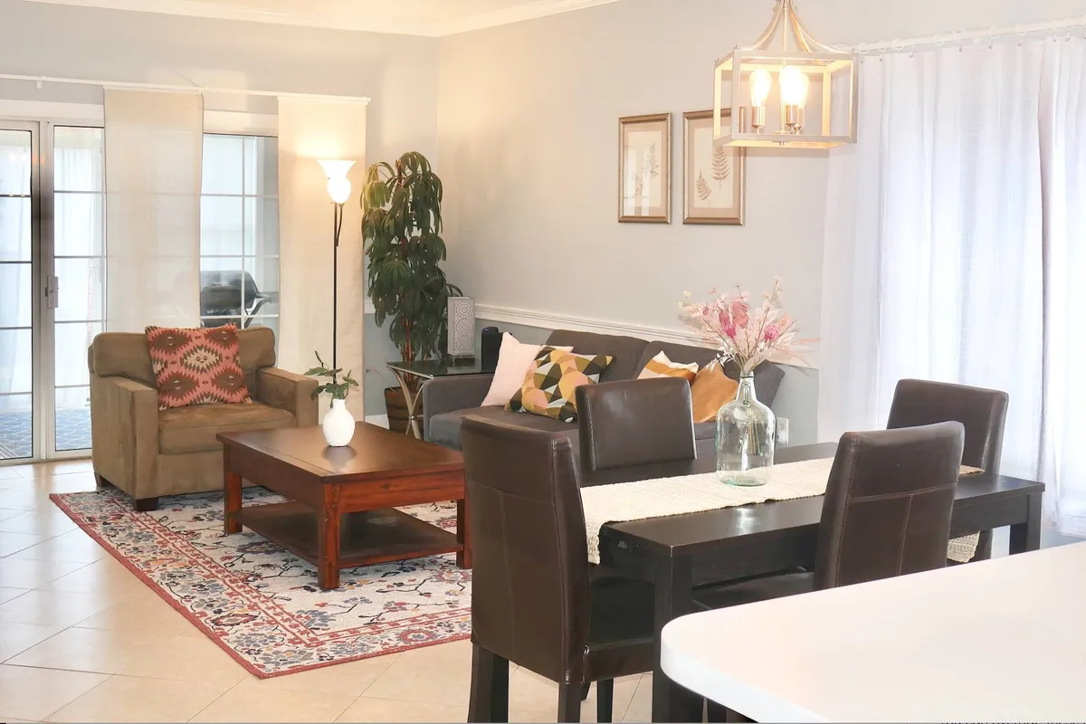 The image showcases a modern, open-concept living and dining area in the condo. A plush sofa and stylish coffee table invite guests to relax, while a chic dining table set, accented by contemporary wall art and a warm floor lamp, creates a welcoming space for gathering and entertaining.